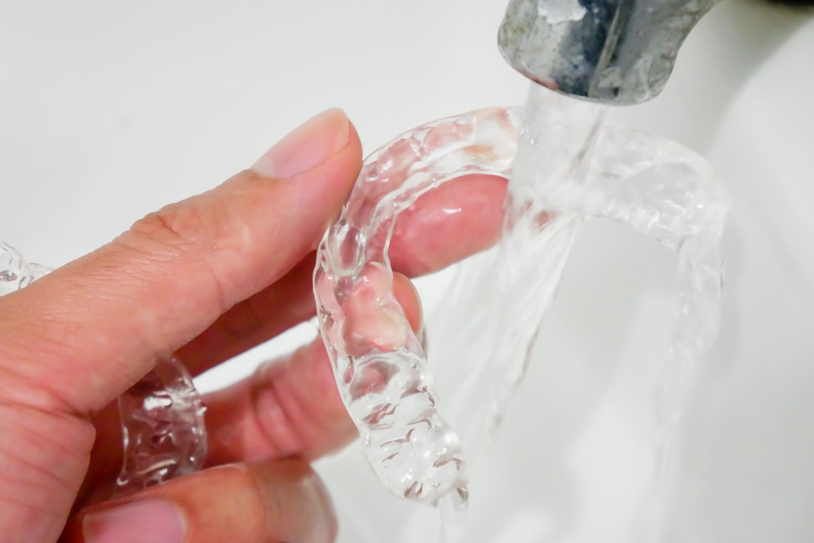 A person holds a toothbrush under running water, emphasizing dental hygiene and orthodontic care with Invisalign aligners.