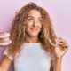 A woman with curly hair holds a tube of toothpaste, promoting straight teeth with Invisalign aligners and orthodontic care.