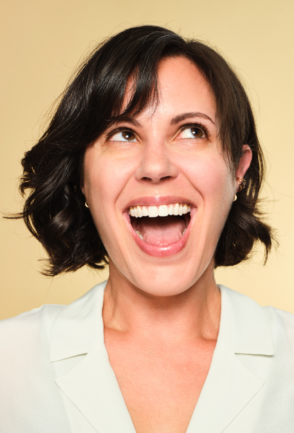 A woman wearing a white shirt, beaming with a big smile, radiating joy and positivity.