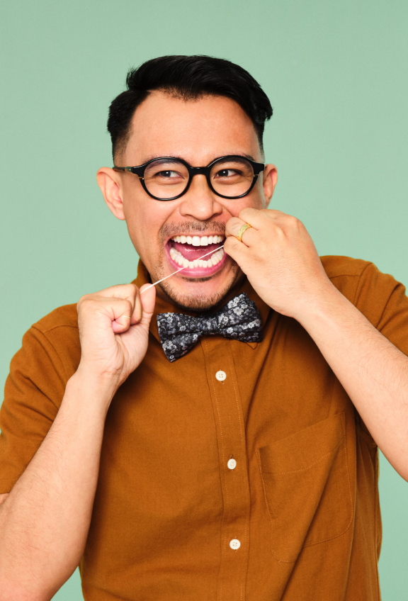 A man wearing glasses and a bow tie is holding a toothbrush, smiling confidently.