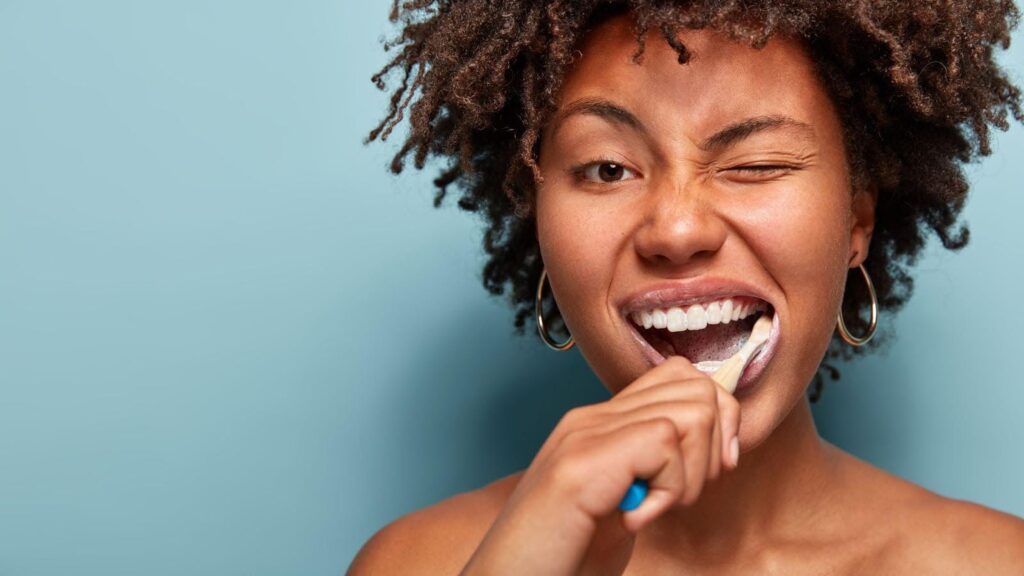 A woman brushes her teeth in a bright bathroom, focusing on dental hygiene